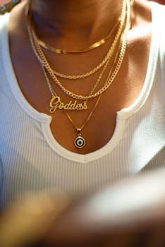 A close-up shot of layered gold necklaces on a woman, featuring a 'Goddess' pendant.